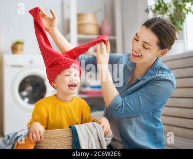 Belle jeune femme et petite fille d'enfant petite aide ont l'amusement et sourire tout en faisant la lessive à la maison. Banque D'Images