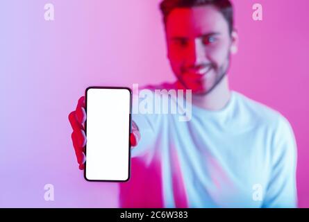 Un millenny tient le téléphone à écran tactile en main avec écran vide dans la lumière néon Banque D'Images