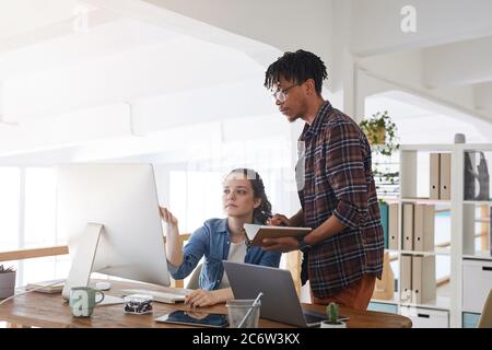 Portrait d'un jeune homme afro-américain qui parle à une collègue féminine en se tenant debout près d'ordinateurs dans un bureau moderne, concept de DÉVELOPPEURS INFORMATIQUES, espace de copie Banque D'Images