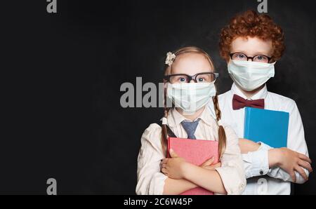 Heureux enfants intelligents étudiant garçon et fille dans le masque médical de protection sur fond noir Banque D'Images