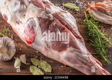 Détail de la hache d'agneau crue sur un panneau de bois avec ail, feuilles de Laurier, romarin et bacon Banque D'Images