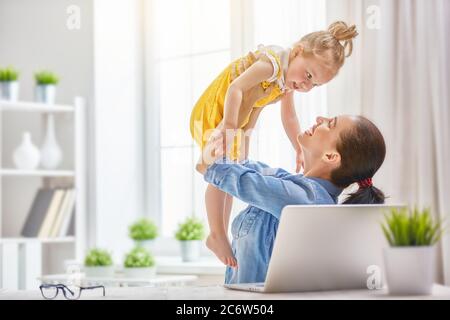 Jeune mère avec enfant en bas âge travaillant sur l'ordinateur à la maison. Banque D'Images