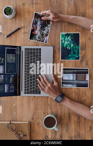 Composition minimale de l'arrière-plan des mains masculines tenant des photos imprimées et utilisant un ordinateur portable sur un bureau en bois texturé, un bureau de photographes, un espace de copie Banque D'Images