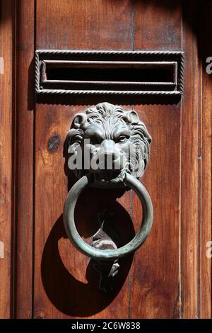 Poignée de porte d'entrée en fer vintage sous forme de tête de lion tenant un anneau et une boîte aux lettres. Volterra. Italie. Banque D'Images