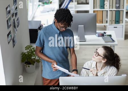 Portrait grand angle de deux jeunes créatifs qui examinent des photos tout en travaillant sur le montage et la publication dans un bureau moderne, dans un espace de copie Banque D'Images