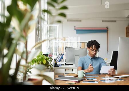 Portrait d'un homme afro-américain créatif qui passe en revue des photos tout en travaillant à l'édition et à la publication dans un bureau moderne, dans un espace de copie Banque D'Images