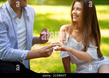 Proposition romantique. Homme millénaire mettant l'anneau sur le doigt de sa belle petite amie dans le parc Banque D'Images