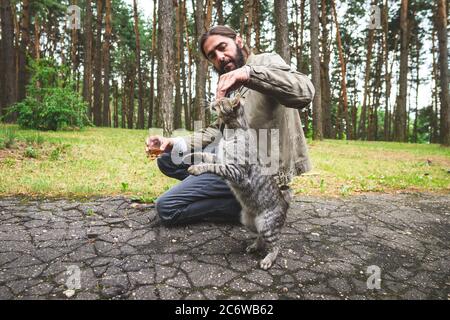 Un homme joue avec un chat tabby gris. Cat fait un tour. Banque D'Images