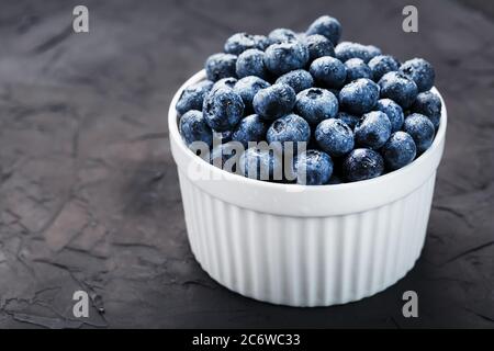 Bleuets biologiques dans une tasse blanche sur un tableau noir. Banque D'Images