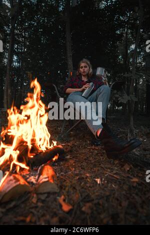 Belle femme de randonnée ayant le repos près de Bonfire après se promener et Randonnée dans la forêt et thé versant dans un mug métallique de Thermos Banque D'Images