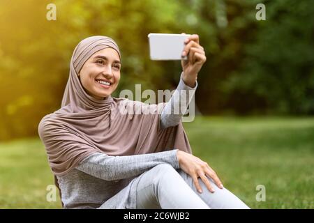 Fille gaie dans hijab emportant le selfie dans le parc public Banque D'Images