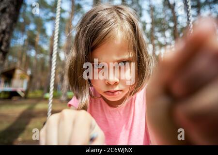 adorable petite fille s'assoit sur une balançoire et fait des visages Banque D'Images