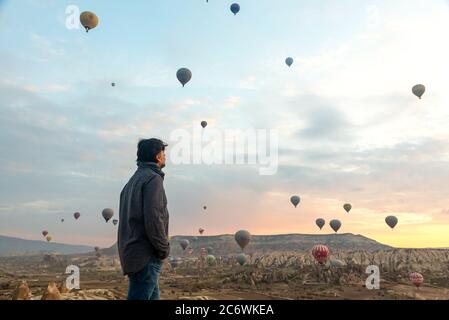 24 février 2018: Homme profitant de la vue sur la vallée avec de merveilleux ballons voler au-dessus de la vallée de Cappadoce. Göreme, Cappadoce, Turquie Banque D'Images