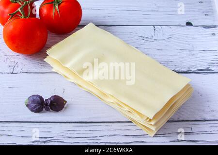 Feuilles de lasagne pâtes avec feuille de tomate et de basilic sur fond de bois. Ingrédients pour une recette italienne. Copier l'espace. Banque D'Images