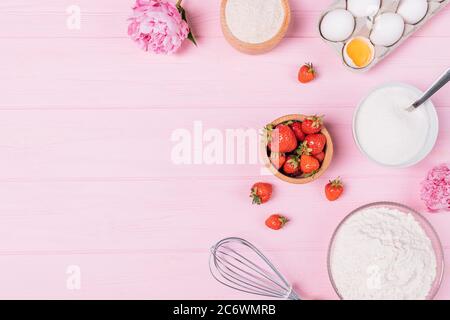 Gâteau aux fraises ingrédients de cuisson, oeufs, farine, sucre, baies fraîches et fleurs de pivoine sur fond rose avec espace libre pour le texte, plat. Banque D'Images