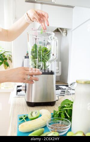 Les mains des filles préparent un smoothie vert, met des feuilles d'épinards frais dans un mélangeur. Concept de saine alimentation. Végétarisme, nourriture végétalienne, nourriture de forme physique, détox, y Banque D'Images