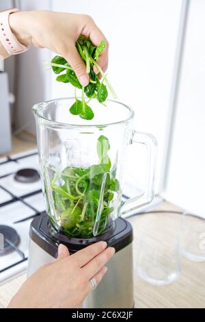 Les mains des filles préparent un smoothie vert, met des feuilles d'épinards frais dans un mélangeur. Concept de saine alimentation. Végétarisme, nourriture végétalienne, nourriture de forme physique, détox, y Banque D'Images