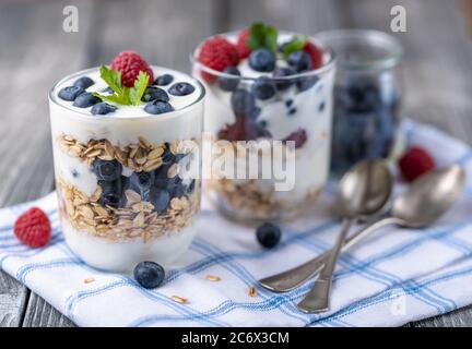 Granola au yogourt blanc aux framboises et aux bleuets dans deux verres sur serviette bleue. Banque D'Images