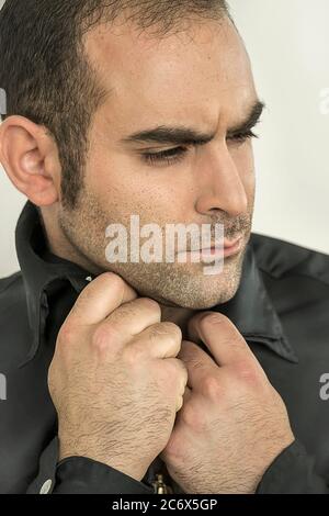 Beau homme méditerranéen posant dans une chemise noire sur fond blanc Banque D'Images