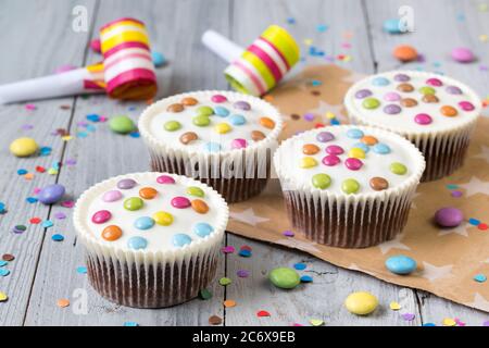 Petits gâteaux avec glaçage blanc et des smarties colorées, cornes et confetti de fête, fond en bois Banque D'Images