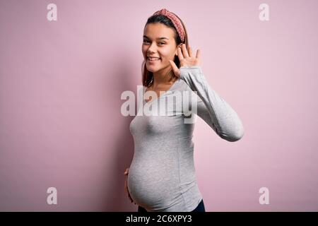 Jeune fille adolescente enceinte s'attendant à bébé sur fond rose isolé Wapouing dire bonjour heureux et souriant, geste de bienvenue amical Banque D'Images