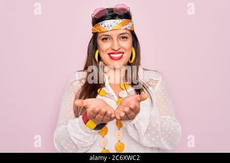 Jeune femme hispanique hippie portant le style boho de mode et des lunettes de soleil sur fond rose souriant avec les mains palmiers ensemble recevoir ou donner gestu Banque D'Images