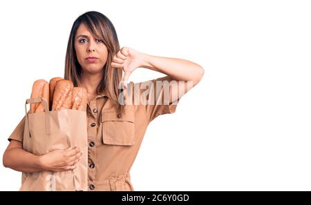 Jeune belle femme tenant sac de papier avec pain visage en colère, signe négatif montrant le désarroi avec les pouces vers le bas, concept de rejet Banque D'Images