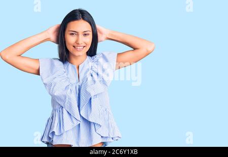 Jeune fille latine belle portant des vêtements décontractés relaxant et étirant, bras et mains derrière la tête et le cou sourire heureux Banque D'Images