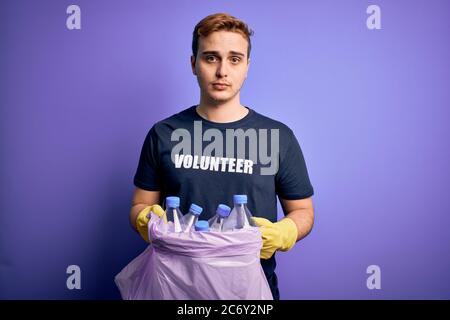 Jeune beau redhead volontaire homme faisant du bénévolat portant un sac avec des bouteilles en plastique pensant attitude et expression sobre regardant confiance en soi Banque D'Images