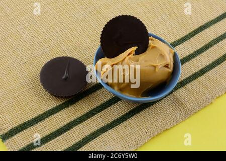 Deux tasses de beurre d'arachide au chocolat noir et le beurre d'arachide dans un bol à trempette bleu sur un tapis de table tissé brun Banque D'Images