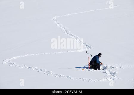 Un homme d'âge moyen pêchant sur glace à Winter, Finlande Banque D'Images