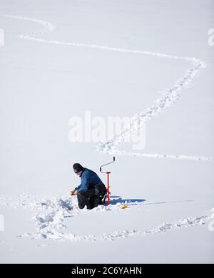 Un homme d'âge moyen pêchant sur glace à Winter, Finlande Banque D'Images