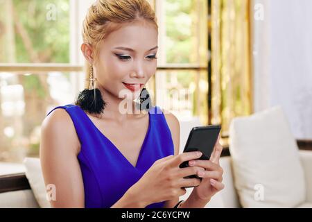 Une jeune femme souriante lit des messages texte de ses amis sur son smartphone Banque D'Images