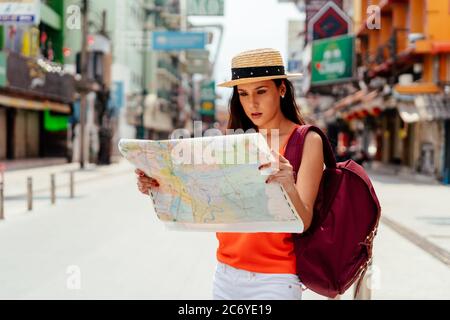 Jeune femme hispanique sérieuse brune tenant une carte dans la rue en vacances avec sac à dos Banque D'Images