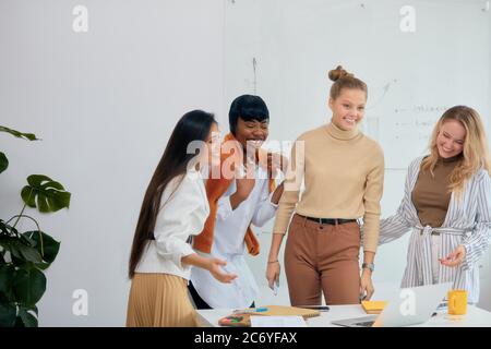 bon travail de quatre femmes diverses travaillant sur un projet d'entreprise au bureau, ordinateur portable sur table. un collègue sympathique, isolé dans un bureau blanc moderne Banque D'Images