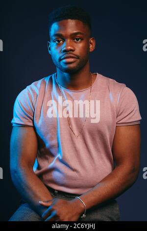 Beau jeune homme à peau sombre vêtu d'une chemise décontractée, posé sur un fond rouge foncé Banque D'Images