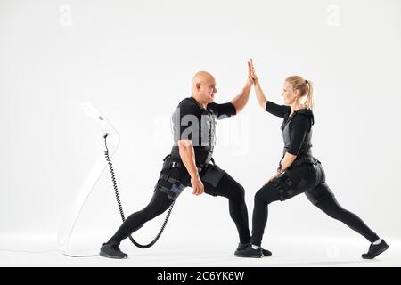 Couple gai portant des combinaisons EMS donnant cinq hauts pendant l'entraînement. Photo pleine longueur. Bon travail, bonne humeur dans le studio de sport. Style de vie Banque D'Images