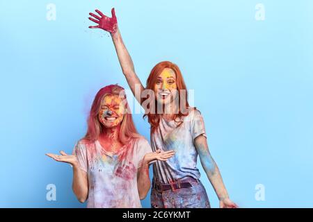 gingembre et blonde filles jouant avec de la poudre colorée.visage et cheveux de femmes trempés dans la couleur et dans un état presque inidentifiable. dos bleu isolé Banque D'Images