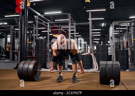 Entraînement sportif de carrossier masculin avec barbell noir lourd dans la salle de gym, se pencher vers l'avant, regardant vers le bas, prêt à soulever, sport et active Life concept, intérieur Banque D'Images