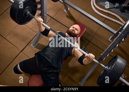 Sportif puissant et brutal, allongé sous une lourde barbell, tenant une barre de fer, les mains en poudre, regardant avec un visage fort, faisant de l'effort, s'entraîner dans la salle de sport Banque D'Images
