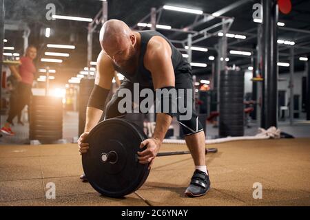 Puissant levier ravie mettant des plaques de poids en métal lourd sur la barbell, faisant des efforts pour s'entraîner dans la salle de gym, se préparant à exécuter l'exercice en train Banque D'Images