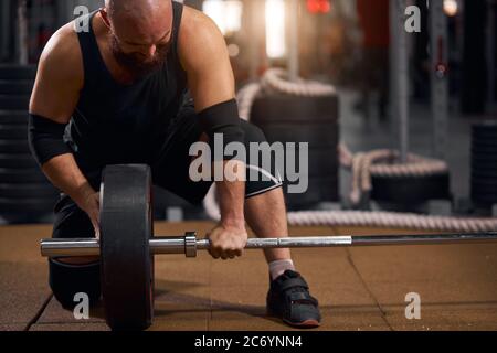 Jeune homme powerlift se préparant à l'impasse de barbell pendant la compétition, passant du temps dans la salle de gym, changeant de barre lourde, concept d'entraînement crossfit Banque D'Images