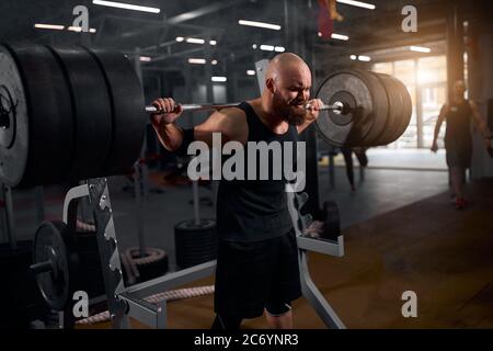 Entraînement sportif de jeune haltérophilie dans la salle de gym moderne utilisant le barbrow, debout près de la barre métallique dans la salle éclairée sombre, se préparant à la compétition de powerli Banque D'Images