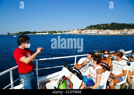 12 juillet 2020, Ria de Vigo, Galice, nord de l'Espagne: Un jeune homme portant un masque prend des photos de ses amis sur le ferry de Vigo aux îles Cies, une destination touristique populaire au large de la côte de la Galice. L'Espagne a assoupli les restrictions de voyage à partir du 21 juin après un verrouillage strict pour contrôler le coronavirus Covid 19 et de nombreux Espagnols reviennent sur les plages. En arrière-plan est la petite ville de Cangas. Banque D'Images