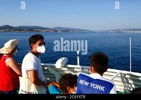 12 juillet 2020, Ria de Vigo, Galice, nord de l'Espagne: Un passager de sexe masculin portant un masque et des lunettes de soleil regarde la vue depuis le ferry entre Vigo et les îles Cies (une destination touristique populaire au large de la côte de Galice). L'Espagne a assoupli les restrictions de voyage à partir du 21 juin après un verrouillage strict pour contrôler le coronavirus Covid 19 et de nombreux Espagnols reviennent sur les plages. Le port de masques est toujours obligatoire dans les transports publics. Banque D'Images