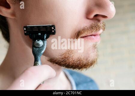 Jeune homme avec barbe rouge et rasoir à la main en gros plan. Sans face. Banque D'Images