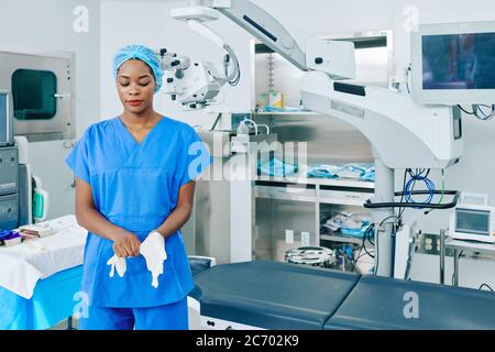 Jeune chirurgien noir mettant des gants en caoutchouc lorsqu'il se prépare à la chirurgie Banque D'Images