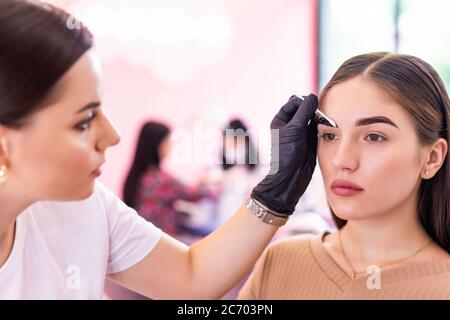 Femme corrigeant la forme des sourcils dans le salon par artiste Banque D'Images