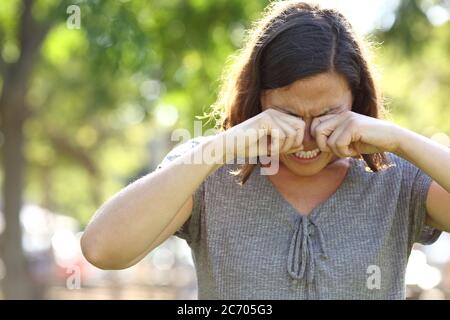 Femme d'âge moyen avec des yeux qui démangent se grattant debout dans le parc en été Banque D'Images
