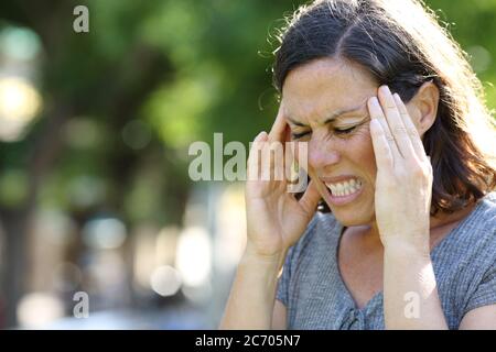 Femme adulte en douleur souffrant de migraine debout dans le parc en été Banque D'Images